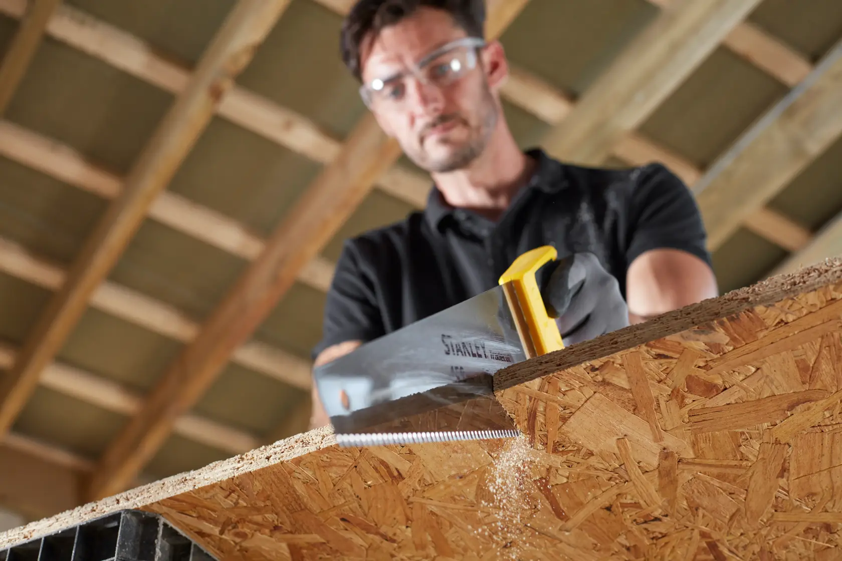 STANLEY STHT20354-1 hand saw with yellow handle, cutting wooden panel in carpentry setting.