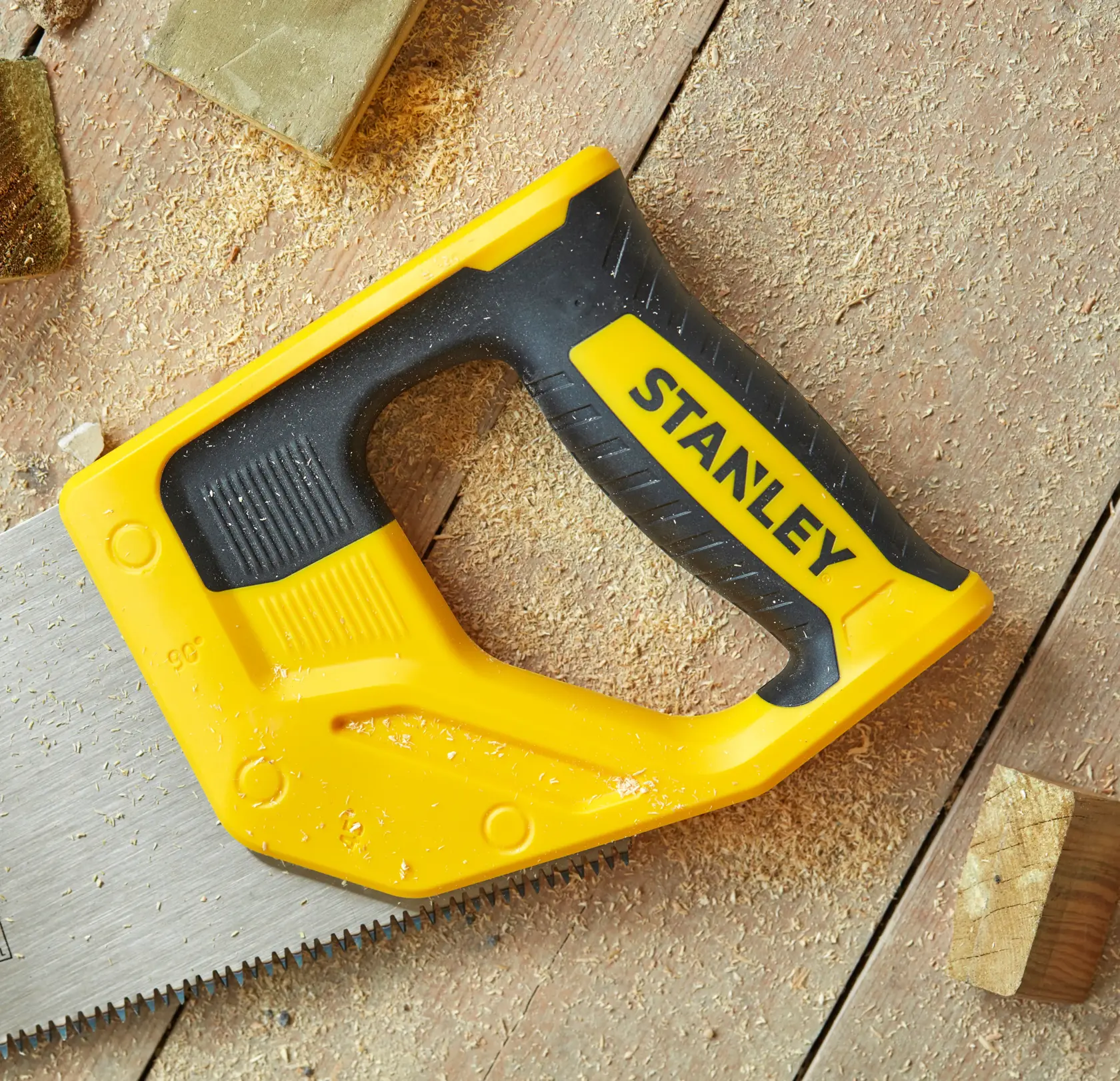 STANLEY STHT20354-1 handsaw with yellow and black handle, top view, lying on wooden surface with sawdust.