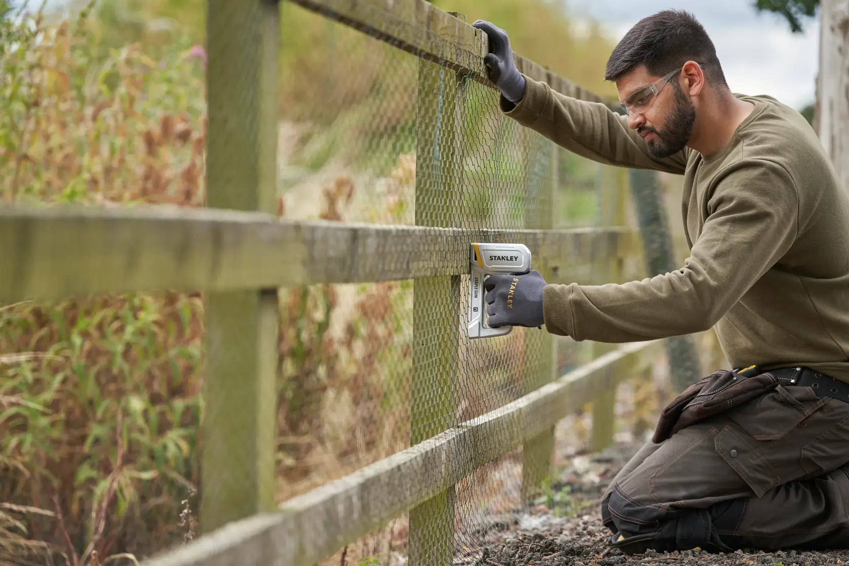 STANLEY STHT70150-0 staple gun in use attaching wire mesh to wooden fence outdoors.