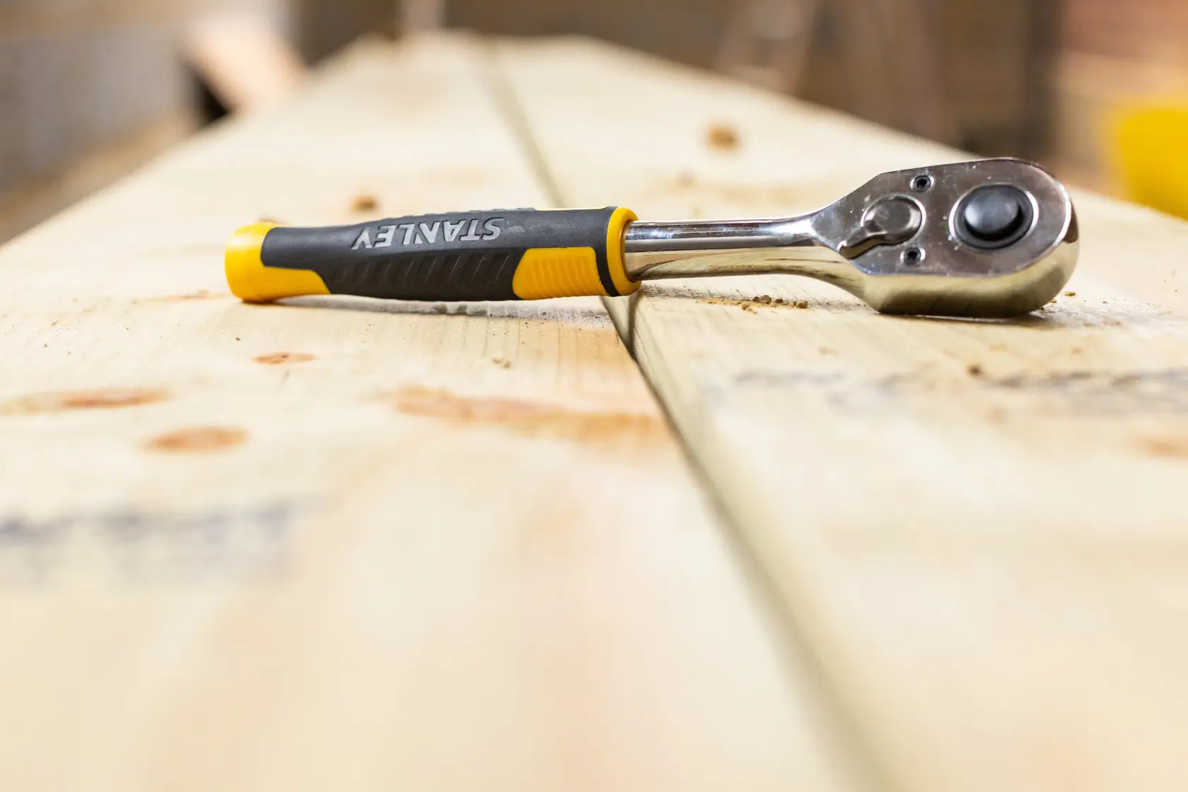 STANLEY STMT82664-0 ratchet wrench with black and yellow handle on wooden boards, close-up photography.