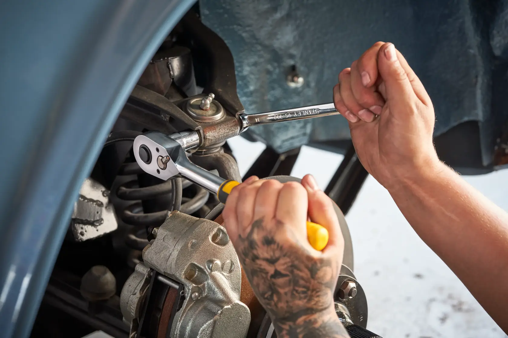 STANLEY STMT82672-0 ratchet and socket set used on car suspension, close-up of hands with tools.