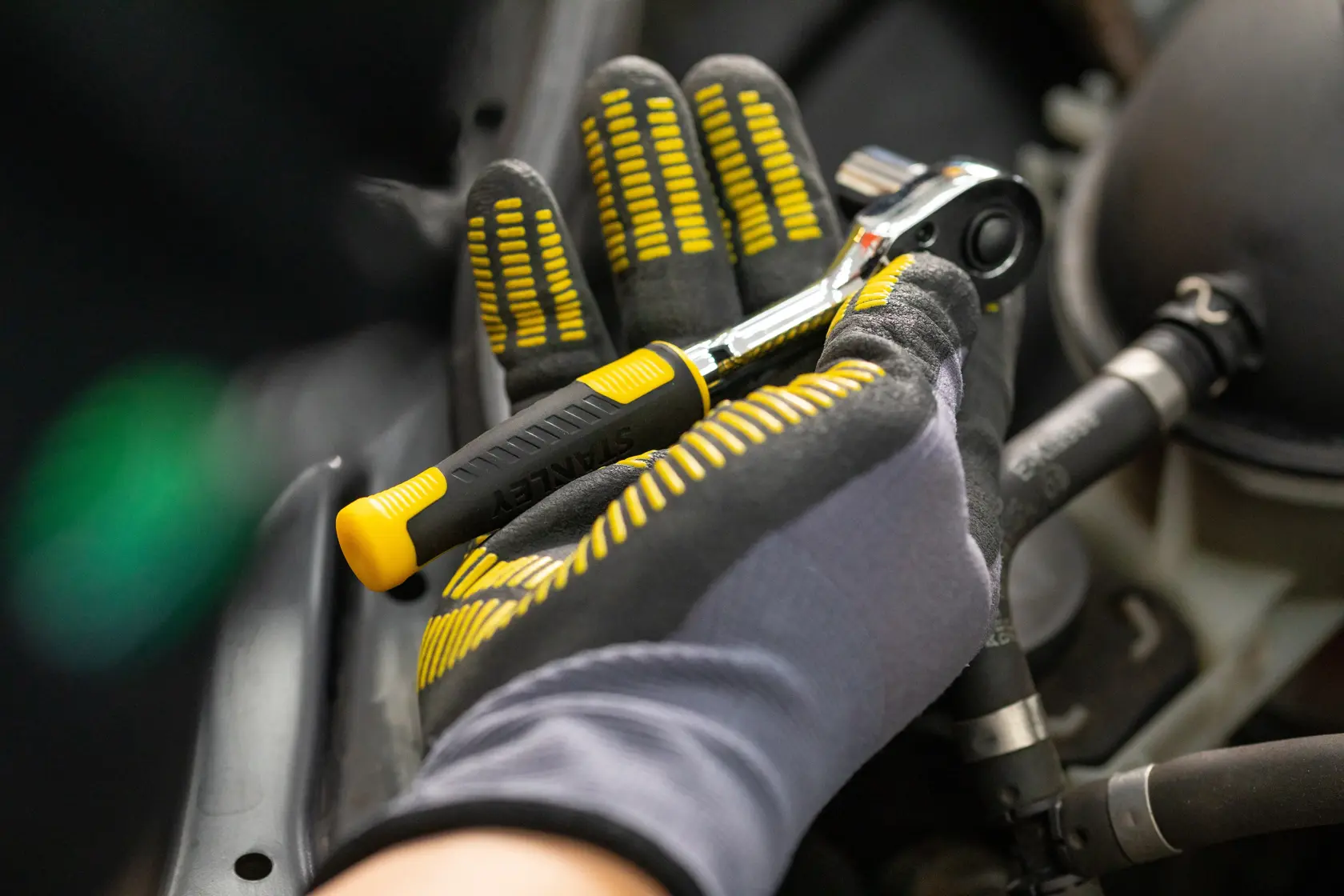 Photo of STANLEY STMT82832-1 ratchet being held in gloved hand during automotive repair.