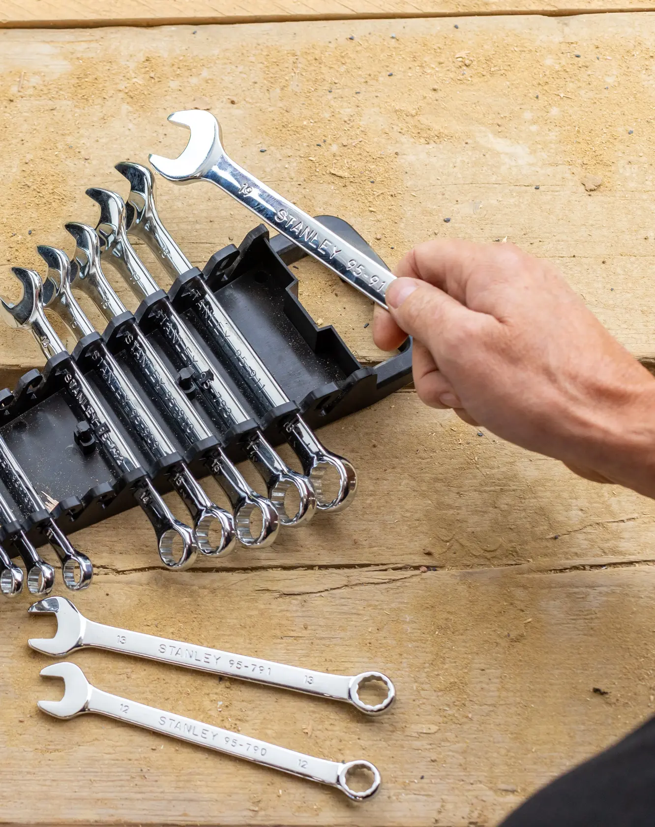 STANLEY STMT82842-0 wrench set in black holder, hand holding one chrome wrench, two wrenches on wooden surface.