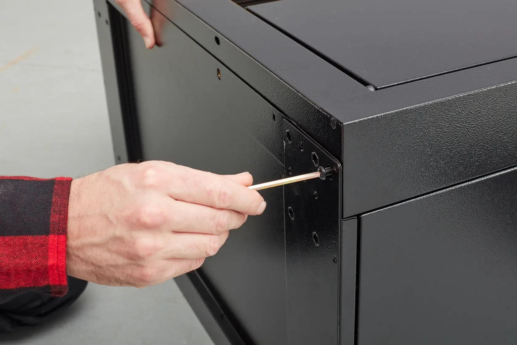 STANLEY STST97595-1 photography of person assembling black metal cabinet with screwdriver, close-up angle.