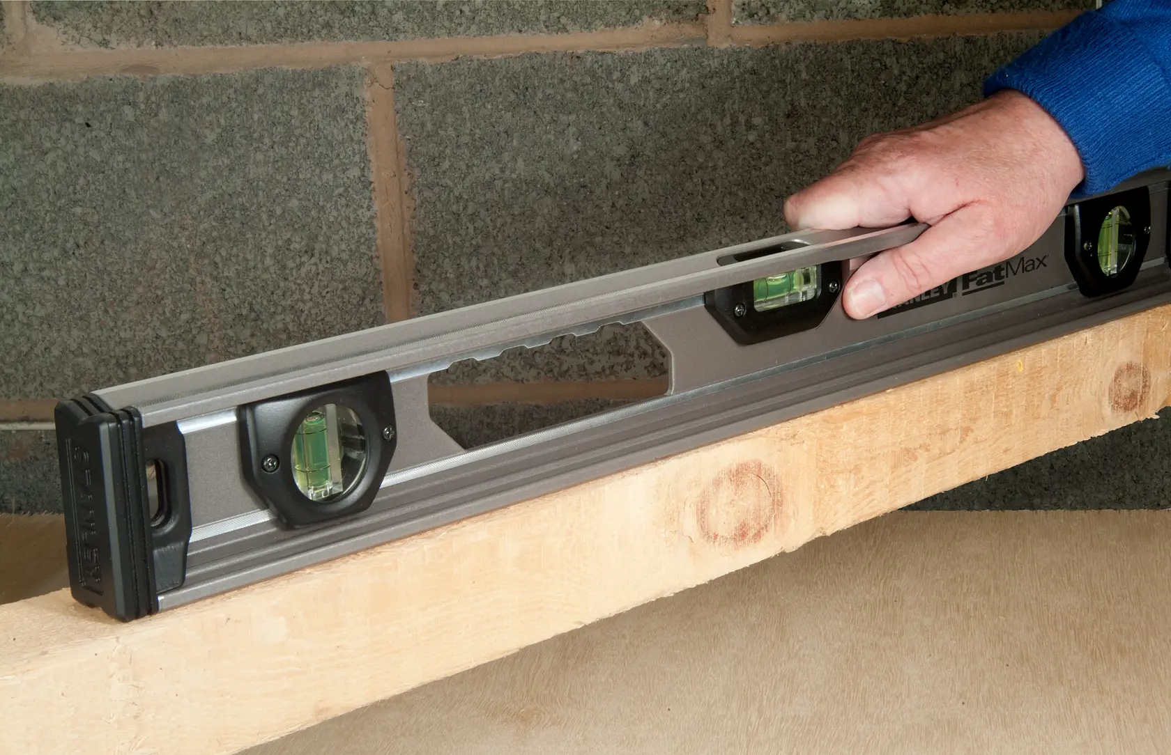 Stanley XTHT1-42131 spirit level held on wood beam, construction context, side angle.