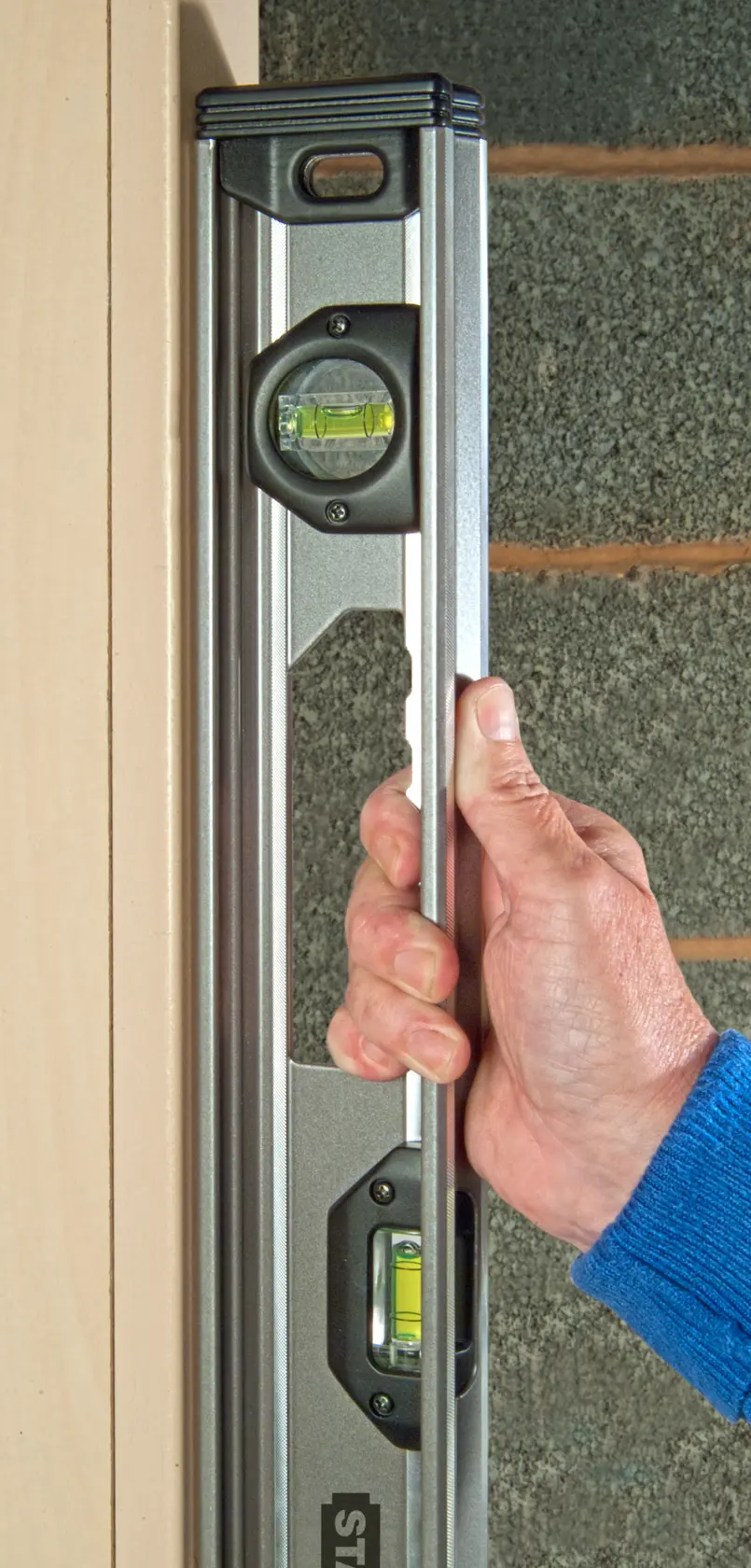 STANLEY XTHT1-42131 spirit level held vertically by hand against door frame.